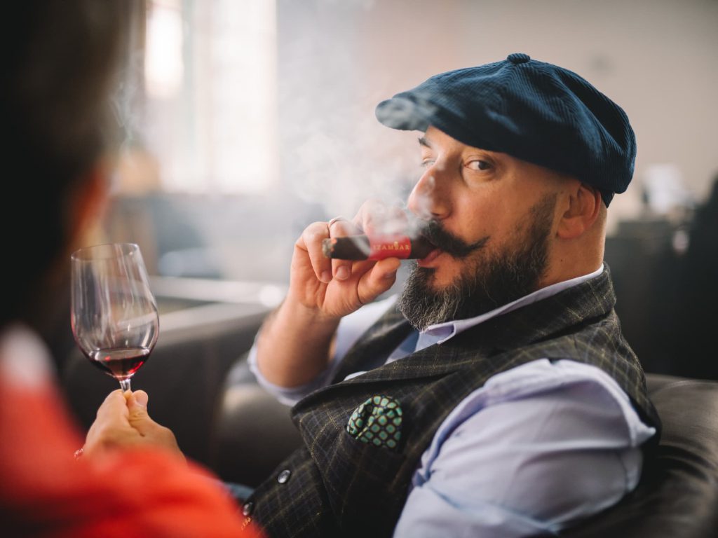 Stéphane Aprille, sommelier du cigare, dégustant un cigare, un verre de vin rouge à la main